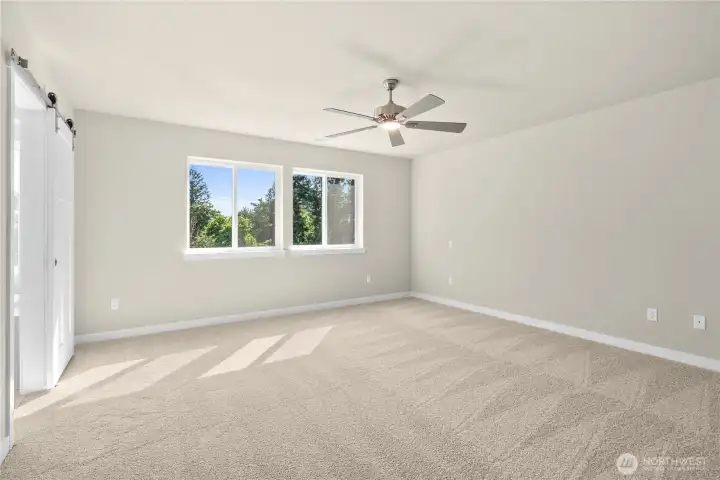 Spacious primary bedroom with carpet flooring creating a soft and calming atmosphere. A ceiling fan with an integrated light fixture is mounted at the center of the ceiling, providing both illumination and airflow.