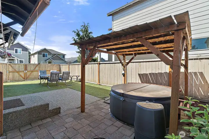 Private backyard retreat featuring a relaxing hot tub, covered pergola, paver patio, and low-maintenance outdoor space designed for year-round enjoyment and entertaining.
