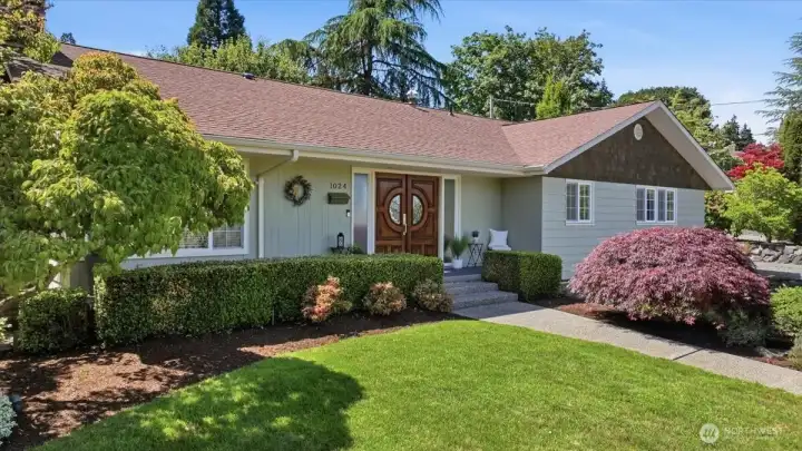Inviting front elevation featuring mature landscaping, manicured lawn, and custom double entry doors.