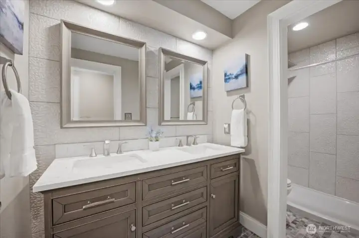 Updated bathroom with double vanity, modern cabinetry, and tiled shower.