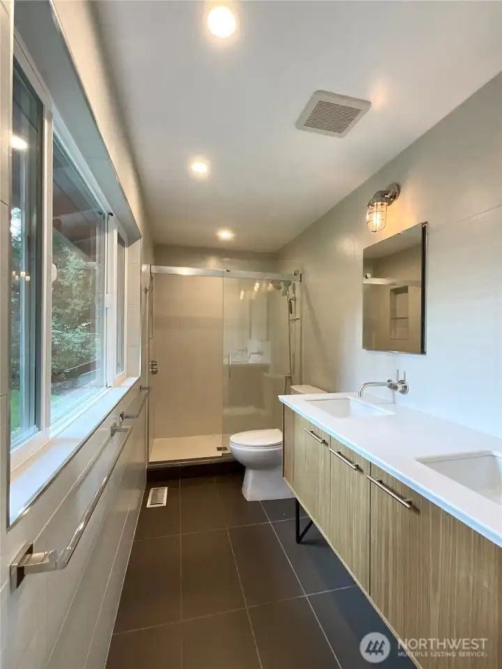 The primary bath with walls of tile, high end fixtures and a floating vanity leading to a custom walk in tile shower. All with great views of the back yard from the oversized window.