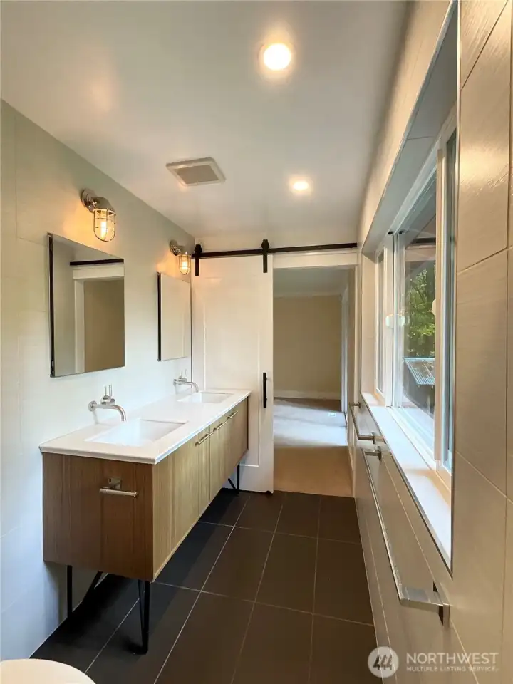 The clean lines of the primary bath amplify its sense of luxury and space featuring  tile all around, a floating style double vanity, spacious walk-in shower and expansive glass that frames a private backyard view.