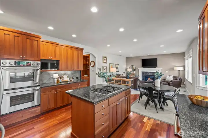 Open layout view from the kitchen into the family room in this Horizon West home for sale in North Gig Harbor, showcasing connected living spaces with warm cherry finishes, gas fireplace, and natural light—perfect for entertaining and everyday comfort.