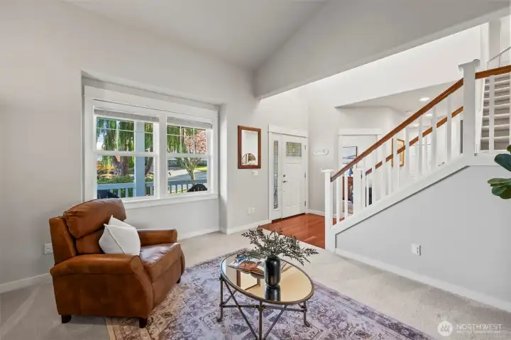 View of living room in Horizon West home for sale in North Gig Harbor looking toward the front entry, highlighting the vaulted ceilings, cherry hardwoods, and glimpse of the covered front porch through large windows for a welcoming first impression.