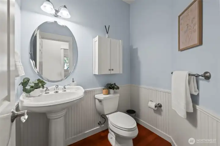 Main floor powder bathroom in Horizon West home for sale in North Gig Harbor featuring classic wainscoting, a pedestal sink, and a private location off the main hallway—combining style and convenience.