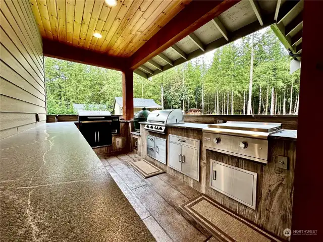 Extend the party to this amazing 17'x11' outdoor kitchen with a gas grill, Traeger, Green Egg, flat top griddle & fridge pull-out!