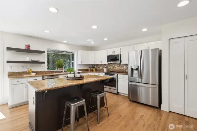 Stylish kitchen with crisp white cabinetry, a central island, and open shelving for display.
