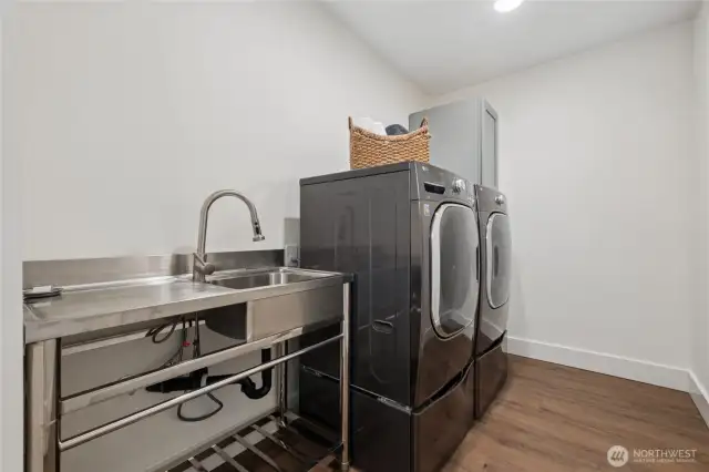 Upstairs laundry room designed for ease, with utility sink, storage cabinet, and front-load machines.