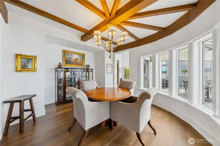 An informal dining alcove with wood-beam ceilings offers sweeping water views and seamless access to the deck and kitchen for indoor-outdoor entertaining.
