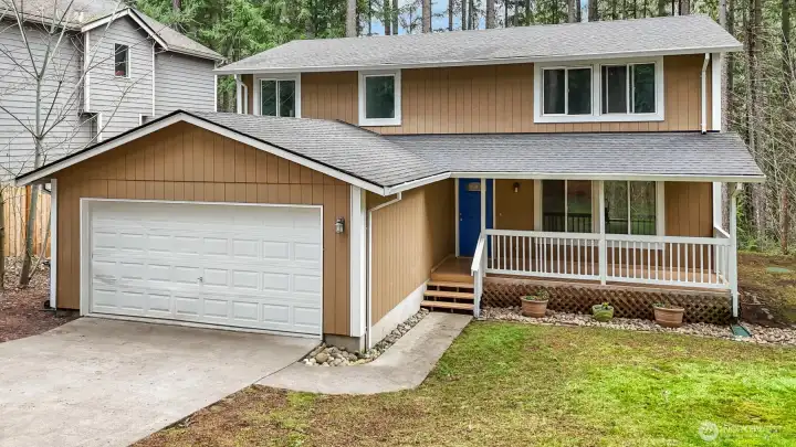 A charming two-story home with a covered front porch, nestled among mature trees.