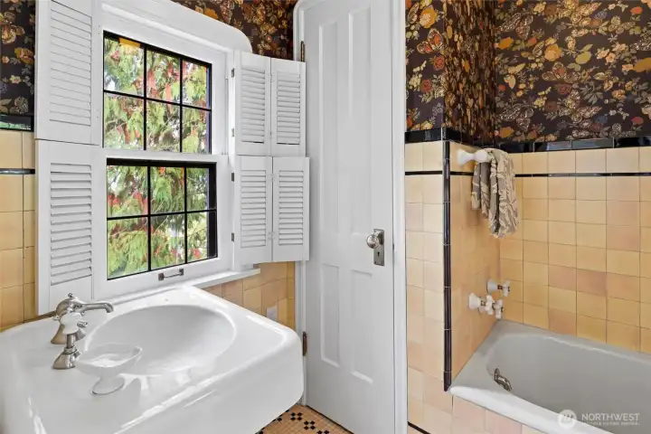 Beautifully preserved 100-year-old primary bathroom, showcasing historic details and timeless character with shutters for privacy and wonderful original tiles.