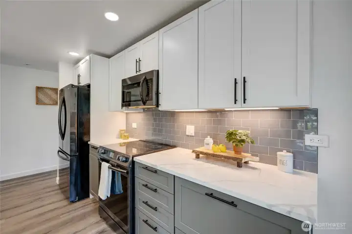 Under-cabinet lighting accentuates the gray subway tile backsplash, adding depth and dimension, while quartz countertops provide a sleek, durable workspace