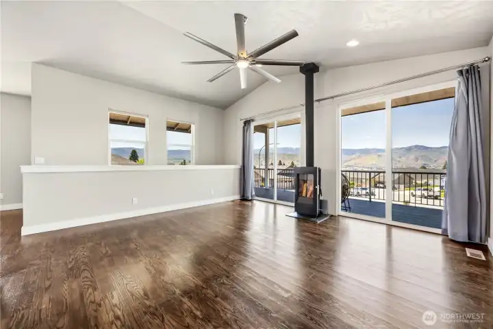 Inviting living room with vaulted ceilings, wood-burning stove, expansive windows, and breathtaking 180-degree valley views