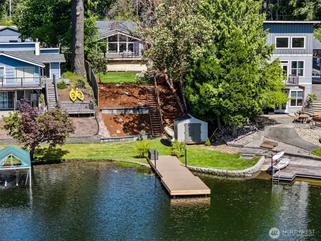 From the Dock to the Deck, Lakeside Living Done Right. This aerial view showcases it all—your own private dock, lush lawn, kayak storage, and a staircase leading up past terraced landscaping to a home that’s all about easy living. And with well-maintained neighbors, the community vibe here is just as welcoming as the view.