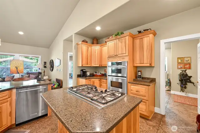 The kitchen features a convection microwave, wall oven, range top and hickory cabinets.   The primary bedroom is to the left of the kitchen and the doorway to the right leads to the laundry room and to the garage.