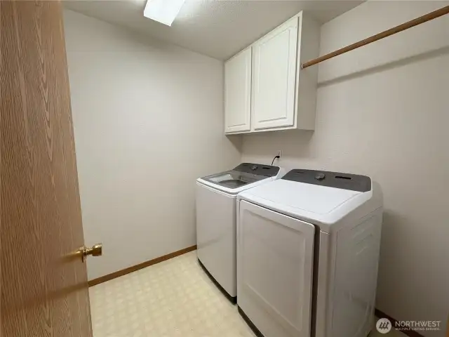The laundry room is equipped with energy-efficient washer and dryer units, a convenient hanging bar, and upper cabinets for extra storage—making laundry day a little easier.