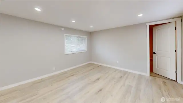 Spacious great room with an open floor plan, featuring warm laminate wood flooring and abundant natural light from new windows dressed with stylish blinds. Fresh interior paint creates a clean, modern feel, while the seamless flow from the kitchen makes this space perfect for entertaining or everyday living.
