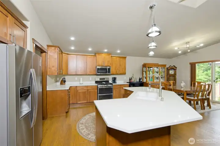 Expansive Chef's kitchen with Quartz countertops, beautiful cherry wood cabinets, stainless steel appliances, luxury vinyl flooring, large walk-in pantry, and a huge island with a breakfast bar.