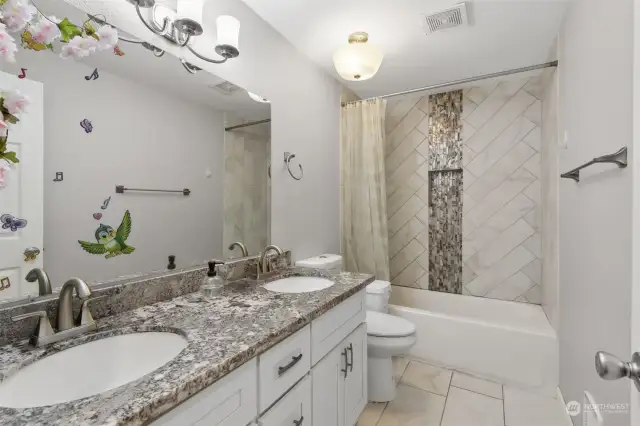 The full bathroom has been updated nicely, with pretty diagonal tile with waterfall-style inlay detail on the shower surround, and double-sink vanity too! Large-scale tile floors and granite countertop add an elegant touch.