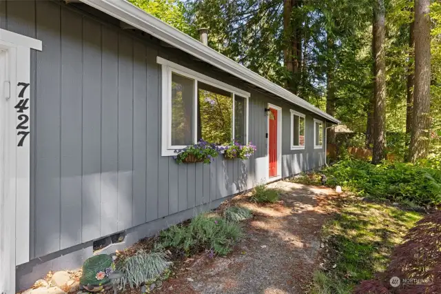 Cute curbside appeal is present thanks to the colorful door and windowsill flower baskets, blooming with summer in front of the sun-dappled walkway to this Evergreen Shores home.