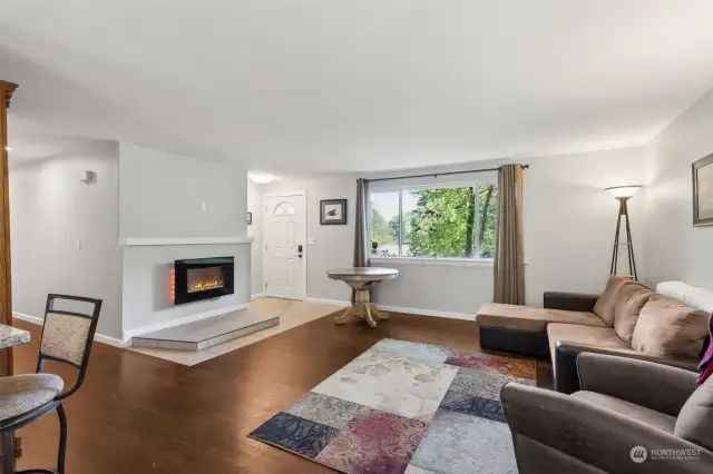 Gorgeous refinished wood flooring sets the tone for this open living room, with cozy electric fireplace for added ambiance. Love seeing a separate entry space into a home with tile flooring to give a durable place to unload shoes and coats.