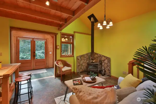 View from the main living space looking back at French door entry. The wood stove creates a toasty warm environment. Loft is above you, bathroom is behind you, stairs to the loft are on the right edge of this photo.