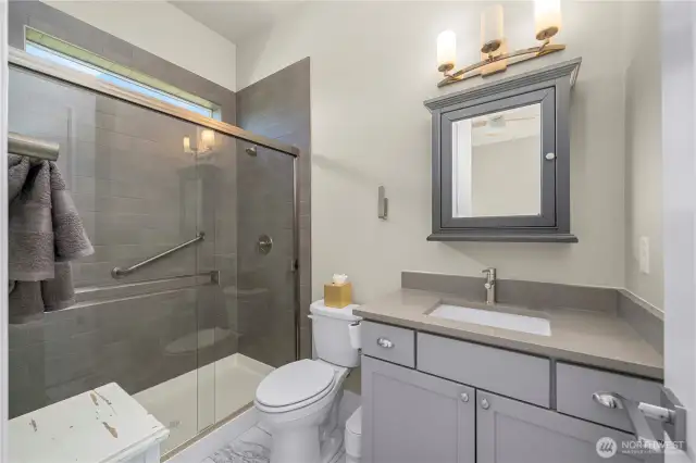 En-suite guest bath with Quartz counters, tile shower surround, tile flooring and a custom framed mirror/medicine cabinet.