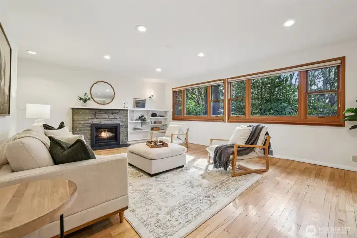 Spacious  living room features gas fireplace & wall of windows with serene forest  views.