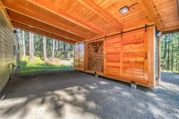 Timber framed lighted carport with firewood storage and enclosed waste bin storage.