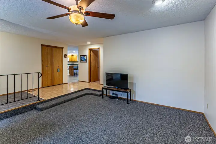 The living room, features a ceiling fan and a wood burning stove. The kitchen is straight ahead.