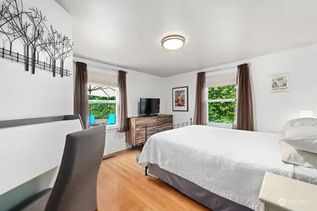 The primary main floor bedroom features Oak hardwood flooring and tranquil green views from both of its windows. It looks out onto the peaceful patio as well.
