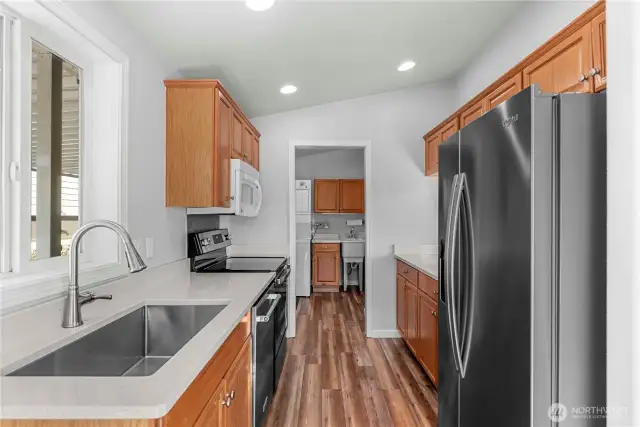 The sellers upgraded kitchen to include quartz countertops and a new sink. Notice utility room with laundry sink ahead.