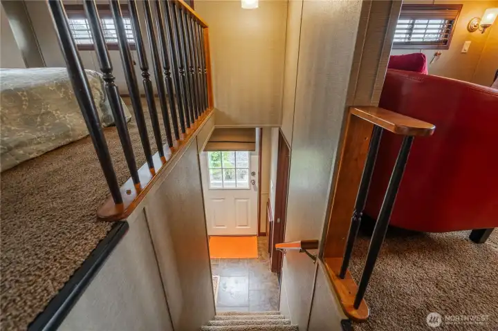 Standing at the top of the stairs and looking down toward the back door. To the left is the second bedroom in the loft area. To the right is the den.