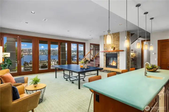 Expansive lower-level entertainment area featuring a stone fireplace, wet bar with quartz countertop, and full-height glass doors opening to the waterfront patio. Enjoy lake and mountain views from this versatile space, perfect for game nights and gatherings.