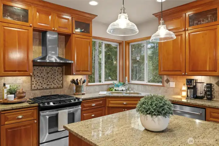 Kitchen boasts center island, serving bar, custom stacked wall cabinetry featuring glass doors to display your treasures, walk in pantry, backyard views, and deck access