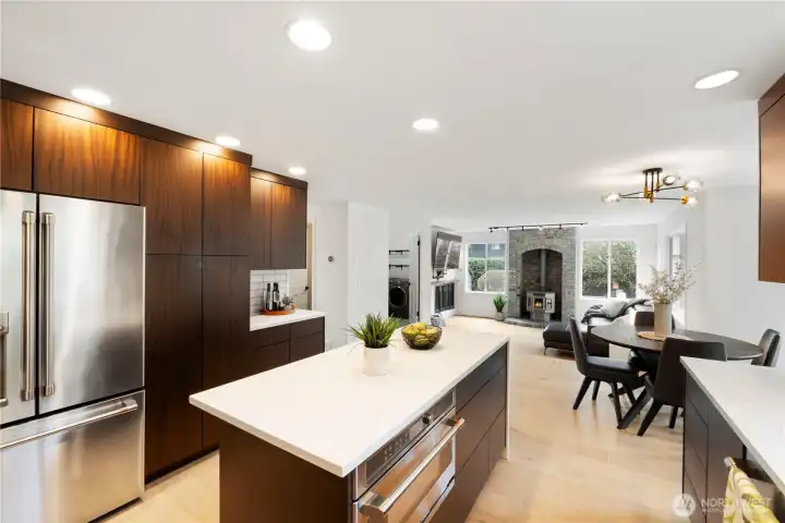 Stunning open-concept kitchen designed for both style and function, featuring rich custom cabinetry, sleek quartz countertops, and a spacious island with built-in microwave/convection oven—perfect for entertaining. Stainless steel appliances and modern finishes create a clean, upscale look, while recessed lighting adds a bright, welcoming feel. The kitchen flows seamlessly into the dining and living areas, highlighted by a cozy fireplace and large windows that fill the space with natural light—ideal for everyday living and gatherings alike.