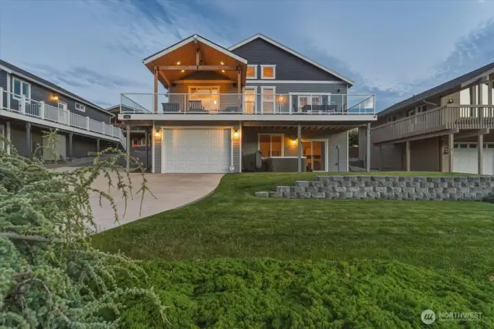 Twilight view of home with grassy front lawn, attached large garage designed to house a wakeboarding boat, golf cart, exercise equipment and more.
