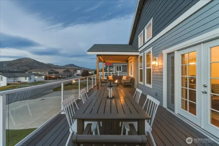 Twilight view of river and mountain view deck with outdoor dining and BBQ area and lounge seating with fire table.