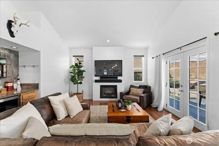 View 4 of Living Room with electric fireplace, mini bar with beverage fridge, board and batten accent wall and French doors leading to the outdoor river and mountain view deck and outdoor living area.
