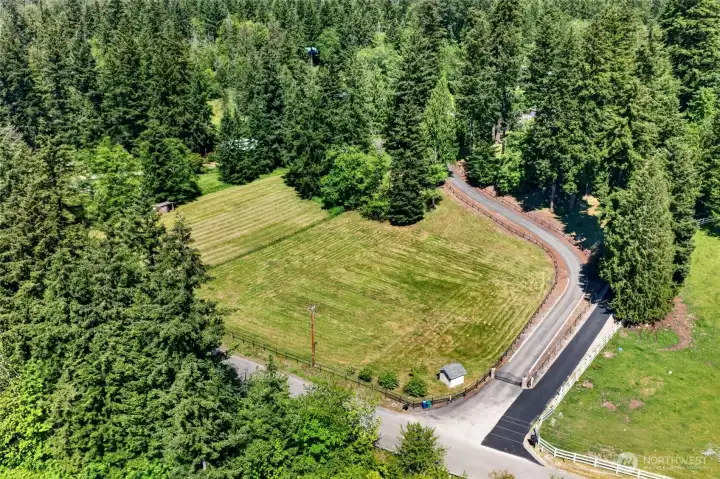 Expansive green pasture and towering evergreens frame the property, offering a peaceful backdrop and natural privacy.