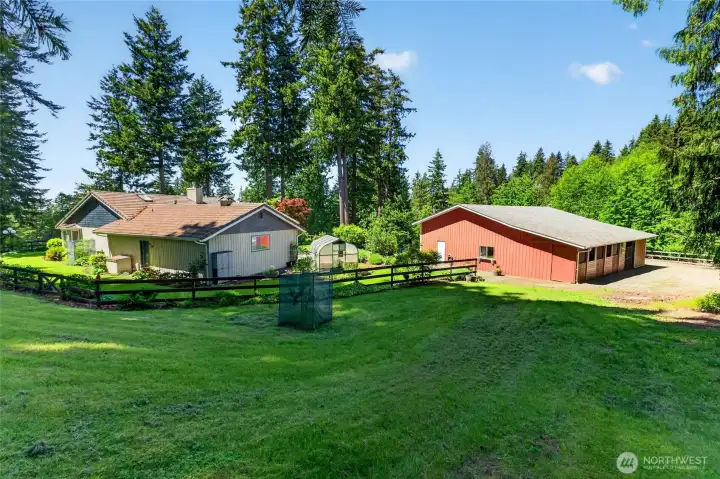 The rear of the home showcases convenient features including a generator located just outside the garage entrance, a charming greenhouse for gardening, and the back of the shop/barn with access to stalls and additional storage.