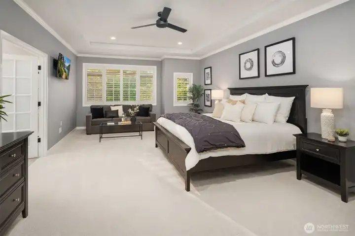 The serene primary suite showcases a signature Murray Franklyn tray ceiling with crown molding, a ceiling fan for year-round comfort, plantation shutters, and a cozy sitting area. A spacious walk-in closet with a custom organization system completes your this retreat.