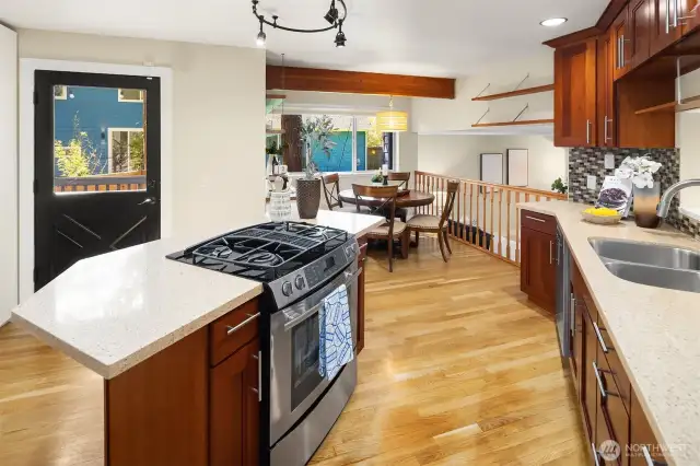 Kitchen with stove in the island, cherry cabinets, and quartz countertops. The kitchen connects seamlessly to a charming breakfast nook.