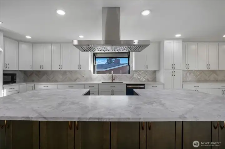Remodeled kitchen with quartz countertops, high-end cabinetry, and large island under statement range hood, positioned to capture natural light and lake views