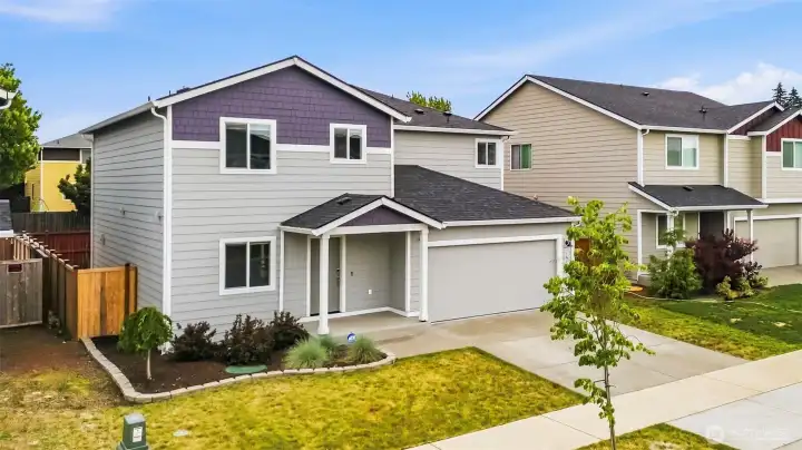 Charming two-story home with crisp white trim, dark plum accent shingles, and a covered front entry. Attached two-car garage, manicured landscaping, and a fresh lawn complete the welcoming curb appeal.