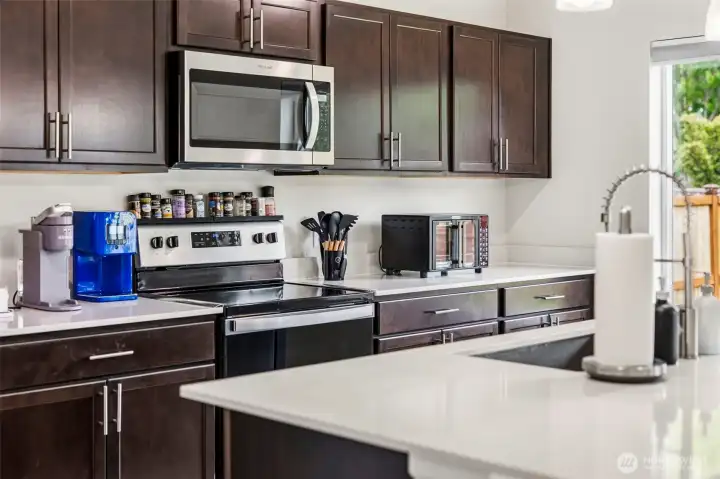 Rich espresso cabinetry paired with quartz countertops and stainless steel appliances, including a smooth-top electric range and over-the-range microwave.