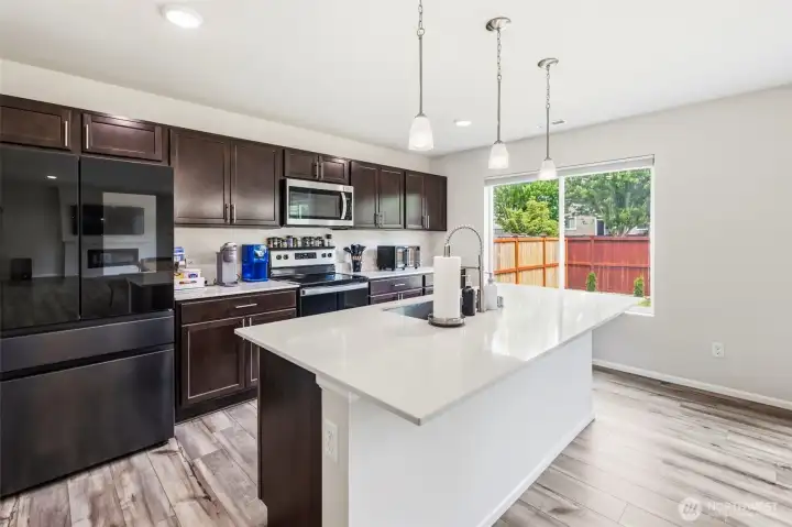 The heart of the home — the island kitchen flows seamlessly into the dining and living areas, anchored by a sleek linear fireplace and filled with natural light.