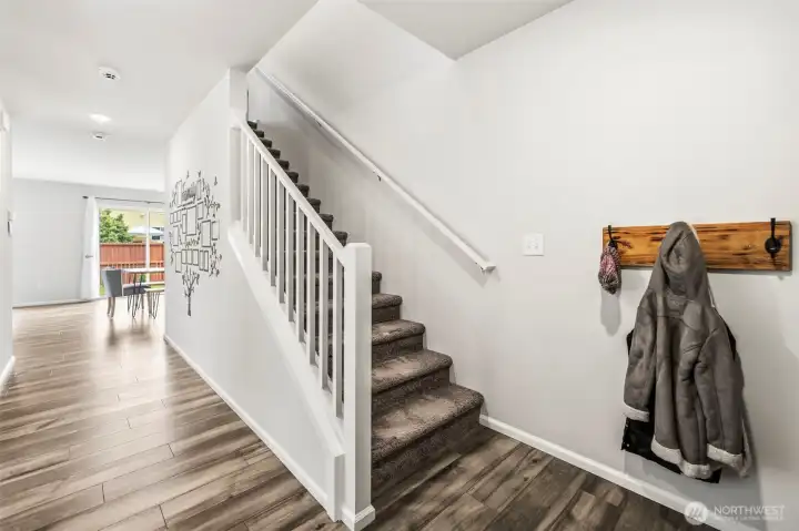 Welcoming entry with wood-look flooring leading to the carpeted staircase and open living areas beyond.
