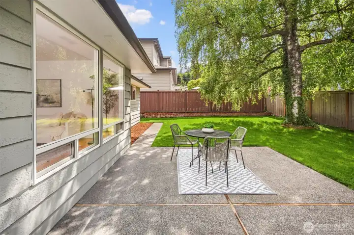 Large yard with large patio and level grass with planting beds at the edge.