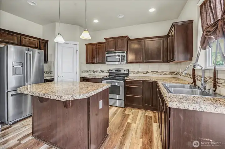 Kitchen with center island, stainless appliances, walk-in pantry with LVP flooring for easy clean up. View of backyard out window over kitchen sink.